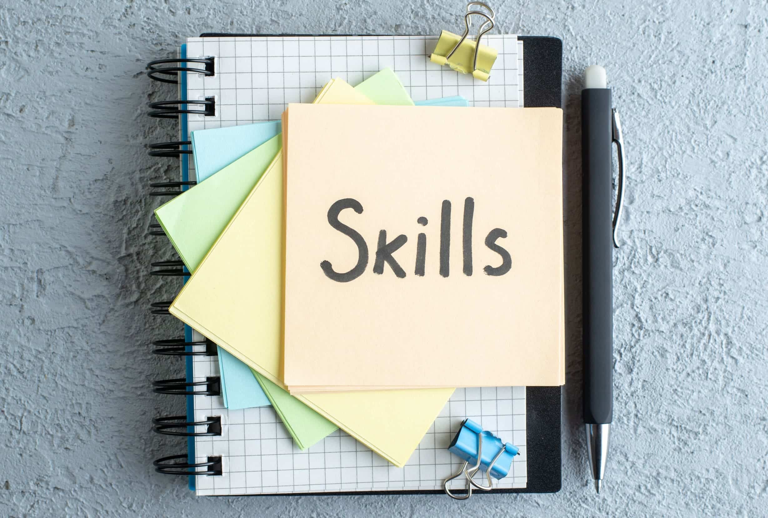 vue-de-dessus-competences-note-ecrite-avec-stylo-et-bloc-notes-sur-fond-blanc-bureau-d-emploi-cahier-d-ecole-salaire-college-business-color